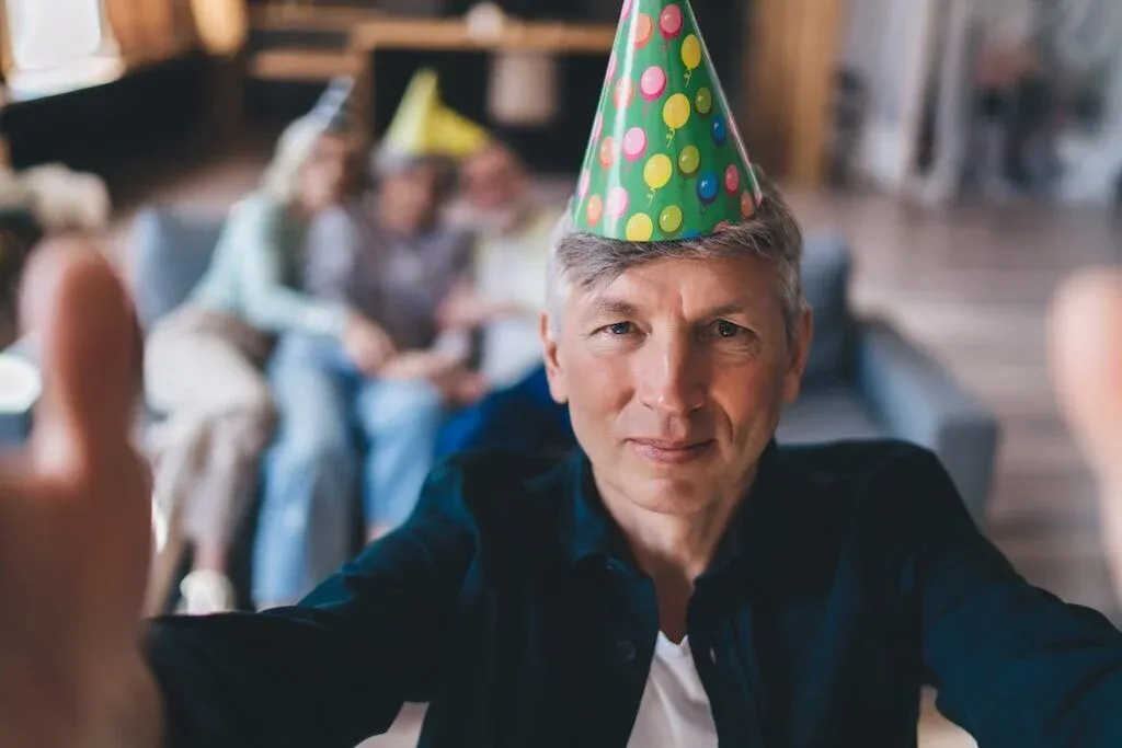 Man wearing a colourful party hat at a gathering.