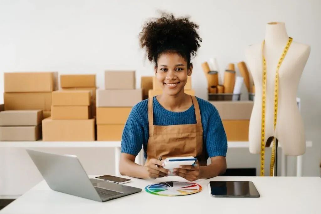 Woman at a workbench with a laptop, fabric swatches and a dressmaking mannequin.