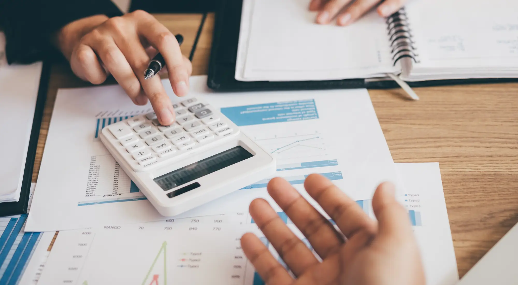 Hands using a calculator beside home loan charts
